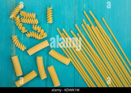 Sélection des matières style italien spaghetti pâtes non cuites et les fusilli rigatoni avec copie espace bleu sur un fond de bois Banque D'Images