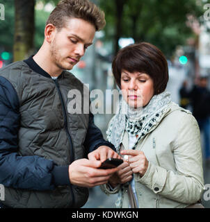 Jeune homme séropositif points la direction avec smartphone à la ville Banque D'Images