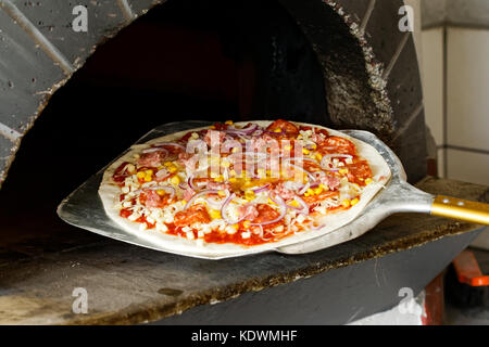 Salami pizza non cuite sur le métal de la pagaie dans l'avant du four à bois. Banque D'Images