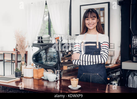 Asian female barista de porter un tablier jean croisa les bras au comptoir bar avec smile face,cafe service concept,propriétaire démarrage d'entreprise Banque D'Images