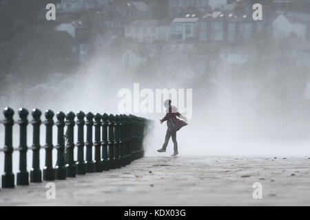 Une femme passe devant les vagues qui s'écrasent sur le mur de la mer à Penzanze, dans les Cornouailles, alors que l'ouragan Ophelia frappe le Royaume-Uni et l'Irlande avec des rafales allant jusqu'à 80 km/h. Banque D'Images
