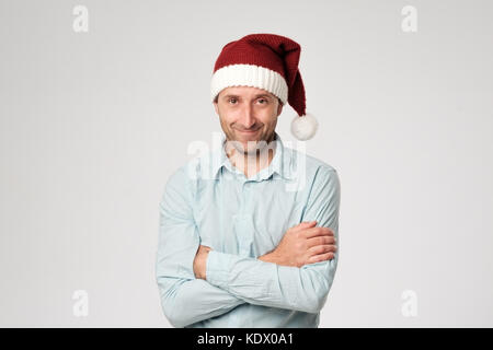 Relaxed mature man wearing santa claus hat standing avec mains croisées sur fond blanc. Banque D'Images