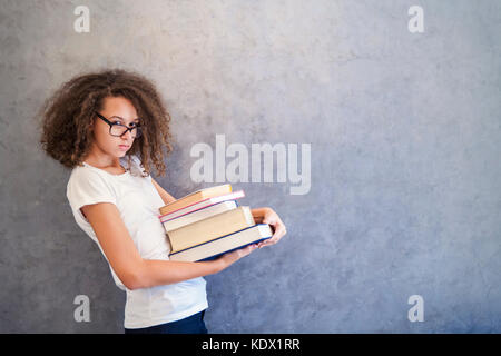 Portrait of teenage girl avec des lunettes se dresse à côté du mur et détient plusieurs livres Banque D'Images