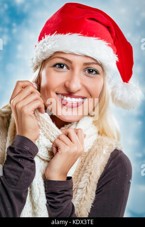 Très jolie jeune femme avec chapeau de Père Noël sur sa tête, souriant à la caméra et à savourer dans son écharpe. Banque D'Images