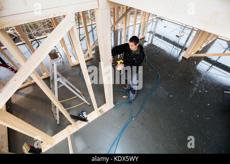 Portrait de jeune menuisier planche en bois forage at construction site Banque D'Images