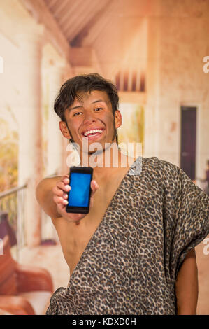 Close up of funny l'homme préhistorique en souriant à la caméra, et en pointant son téléphone cellulaire à l'avant, dans un arrière-plan flou Banque D'Images