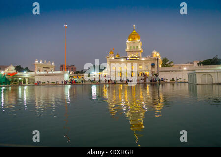 Delhi, Inde - le 19 septembre 2017 : marche des personnes non identifiées, en face des principaux sanctuaires sikh de Delhi - gurudwara Bangla Sahib. Le bâtiment principal du temple est éclairé et est reflétée dans l'eau de l'étang sarowar en Inde. Banque D'Images