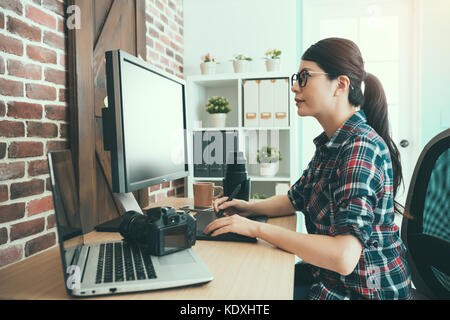 Belle sweet Femme photographe à la recherche de travail sur l'examen de l'ordinateur à l'aide d'image et retouche numérique stylo assis sur l'édition de bureau. Banque D'Images