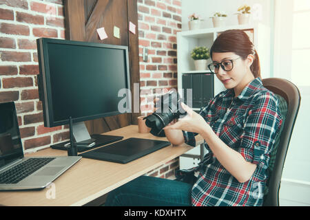 Jolie femme photographe élégant appareil photo d'affaires de l'examen et le choix de photo pour l'édition photo retouch sitting on office 24. Banque D'Images