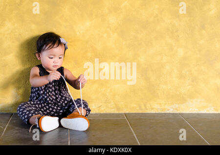 Cute asian toddler essayer de porter ses propres chaussures brunes. bambin essaie d'attacher sa propre chaussure. Mettez vos propres chaussures jour Banque D'Images