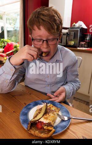 Jeune garçon mangeant une crêpe pour le petit déjeuner Banque D'Images