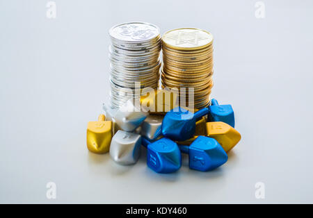 2 piles de pièces en or et argent hanukkah entouré par de minuscules dreidels isolé sur un fond plein Banque D'Images