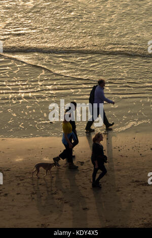 Une famille à marcher ensemble sur une plage au coucher du soleil avec leur chien pagayer dans les eaux peu profondes avec les vagues à leurs pieds. Banque D'Images