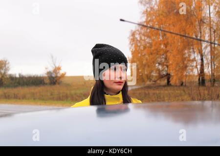 Temps d'automne : belle fille dans un manteau jaune posant contre une forêt de bouleaux d'automne. Banque D'Images