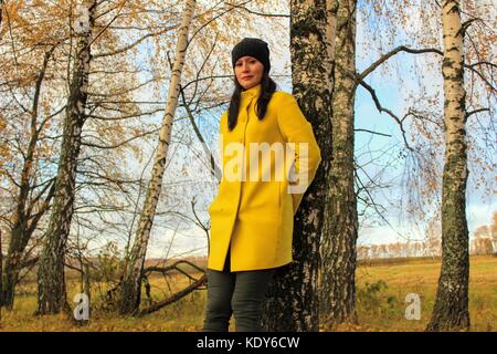 Temps d'automne : belle fille dans un manteau jaune posant contre une forêt de bouleaux d'automne. Banque D'Images