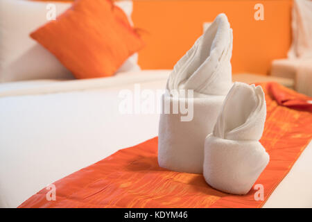 Origami serviette disposée sur un lit dans la chambre de couleur orange Banque D'Images