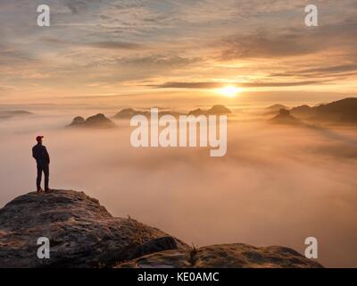 Moment de solitude sur le sommet rocheux exposés. man in black profitez d'une vue merveilleuse. s'asseoir sur le randonneur pic de roche et de regarder dans la brume et le brouillard coloré Banque D'Images