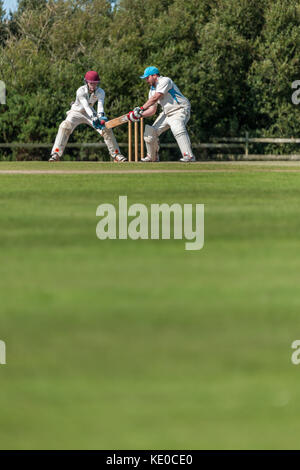 Un batteur joue un coup au cours d'un match de championnat dimanche entre deux équipes de cricket locaux. Banque D'Images