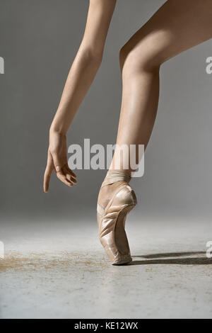 Ballerine offres pose dans le studio sur le fond gris. Elle se tient sur l'orteil et détient le bras à côté de la jambe. girl porte des chaussures pointe beige Banque D'Images