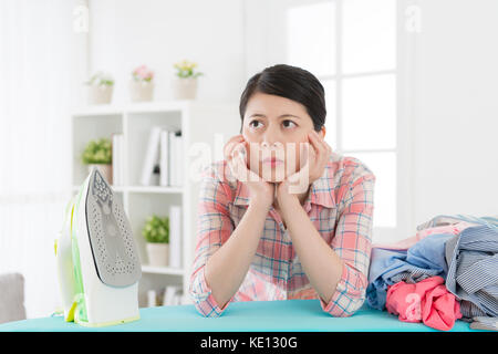 Jolie femme au foyer élégant vêtements repassage sentiment ennuyeux et s'appuyant sur la réflexion du conseil comment vite faire des travaux ménagers. Banque D'Images