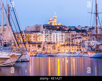 Yachts se reflétant dans les vieux vieux port de Marseille sous notre dame de Paris, France, par nuit. Banque D'Images