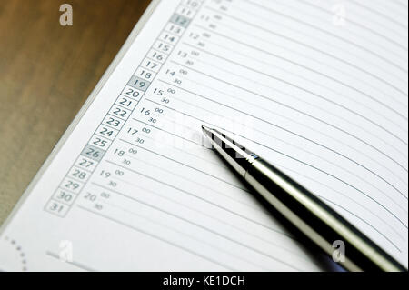 Vue rapprochée d'un stylo en métal se trouvant sur le journal d'un calendrier sur un mat en bois Banque D'Images