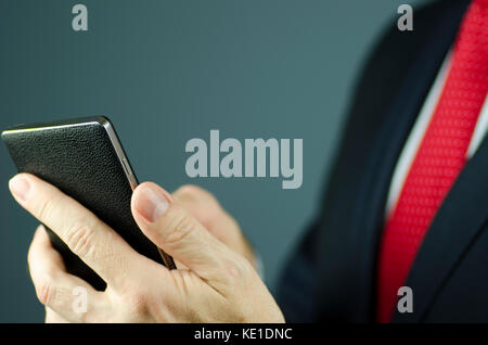 Vue rapprochée de manager en costume avec cravate rouge holding smartphone avec étui en cuir Banque D'Images
