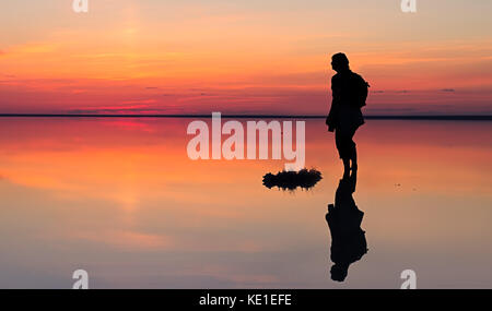Silhouette de l'homme seul à la dynamique vers le coucher du soleil reflétée dans les eaux peu profondes du lac solt Banque D'Images