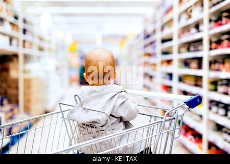 Cute little baby au supermarché. bébé assis dans le panier. vue arrière. Banque D'Images