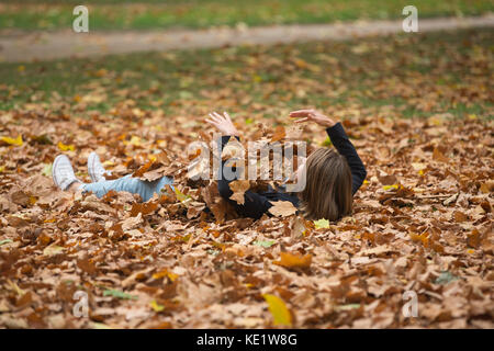 Une jeune femme se trouve entre les feuilles de l'automne à St James Park tandis que son partenaire prend une photo avant de le soulever dans ses bras, Londres, Angleterre, Royaume-Uni Banque D'Images