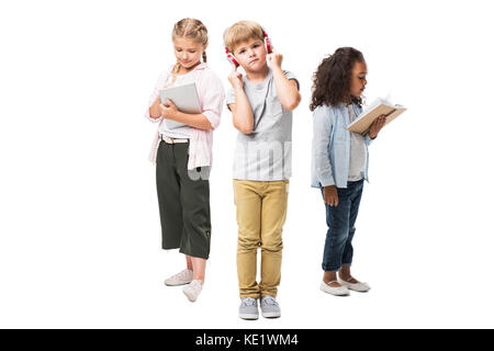 Adorable Kids multiethnique à l'écoute de la musique dans les écouteurs, using digital tablet and reading book isolated on white Banque D'Images