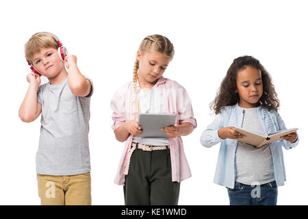 Adorable Kids multiethnique à l'écoute de la musique dans les écouteurs, using digital tablet and reading book isolated on white Banque D'Images