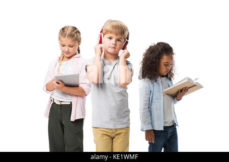 Adorable Kids multiethnique à l'écoute de la musique dans les écouteurs, using digital tablet and reading book isolated on white Banque D'Images