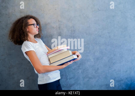 Portrait of teenage girl avec des lunettes se dresse à côté du mur et détient plusieurs livres Banque D'Images