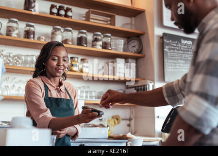 Client en utilisant une carte bancaire et la technologie nfs de payer un barista pour un achat dans un cafe Banque D'Images