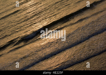 Le soleil qui se reflète dans une mer chatoyante avec des vagues et des galets marins et atmosphériques mouvement donnant Banque D'Images