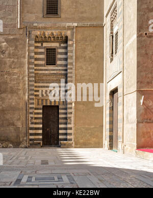 Porte de bois entouré de noir et blanc à rayures en décorations et stone wallat la cour du sultan Hassan mosquée, Le Caire, Egypte Banque D'Images