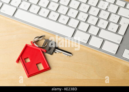 Chambre rouge chambre porte clé avec chaîne et pendentif clé clavier de l'ordinateur sur un bureau en bois - Location de maison ou d'acheter en ligne concept Banque D'Images