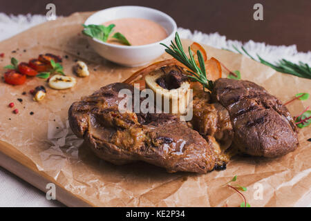 Le grand morceau de viande rôtie sur l'os avec la sauce et les épices sur planche de bois Banque D'Images