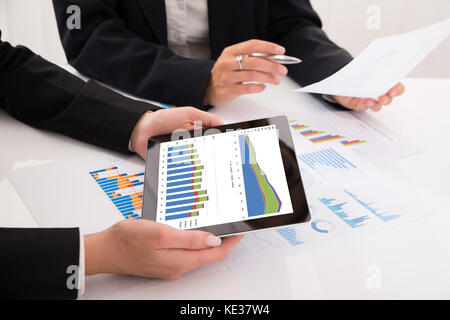 Close-up of young comparer les graphiques de digital tablet in office Banque D'Images