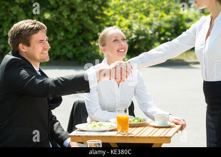 Businesswoman looking at businesspeople shaking hands in restaurant Banque D'Images