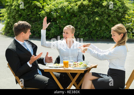 Businesspeople having argument dans restaurant avec de la nourriture et verre de jus sur la table Banque D'Images