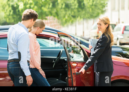Jeune femme heureuse nouvelle d'ouverture de porte de voiture rouge pour le client Banque D'Images