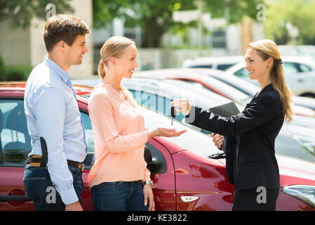 Vue latérale du concessionnaire femelle donnant à clé de voiture couple heureux Banque D'Images