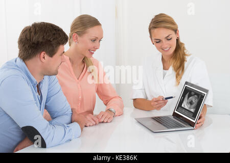 Femme Médecin montrant Échographie de bébé pour jeune couple heureux On Laptop Banque D'Images