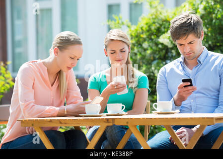 Groupe d'amis à l'aide de téléphone mobile avec la tasse de thé sur la table Banque D'Images