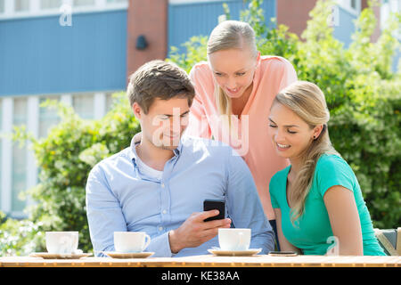 Groupe de professionnels jeunes amis Looking At Mobile Phone In Cafe Banque D'Images