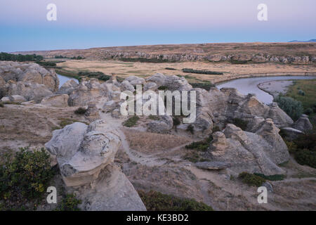 Des formations rocheuses, des cheminées et la rivière Milk après le coucher du soleil au parc provincial Writing-on-Stone, Alberta, Canada. Banque D'Images