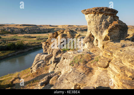 Des formations rocheuses, des cheminées et la rivière Milk au lever du soleil en parc provincial Writing-on-Stone, Alberta, Canada. Banque D'Images