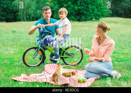 Femme à la recherche d'un homme d'enseigner son fils à faire du vélo dans la région de Park Banque D'Images